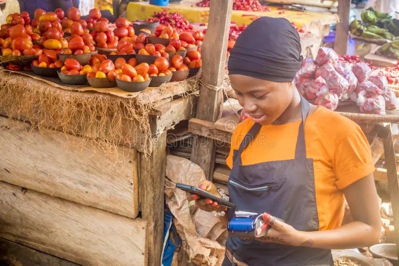 Une vendeuse de marché consulte son téléphone derrière son étal
